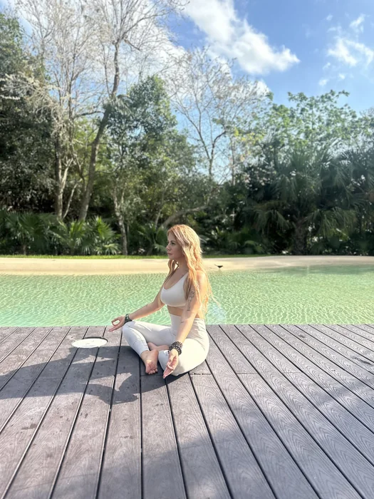 Agi Kali sentada en postura de meditación junto a una piscina rodeada de vegetación